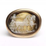 Horizontal oval cameo. White over pale brownish grey layered agate. Depicts Cupid in a Biga